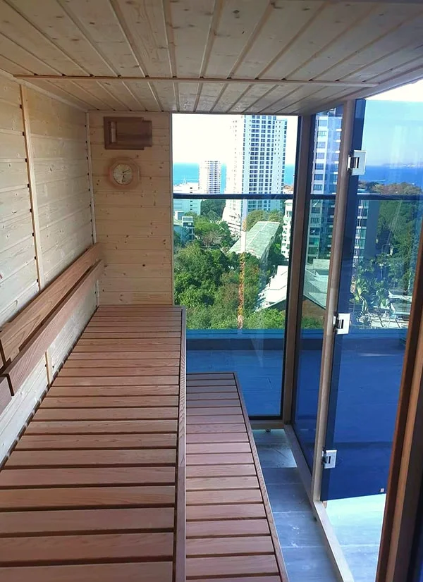 Compact cedar sauna on a high-rise condominium balcony, city and sea skyline through the glass