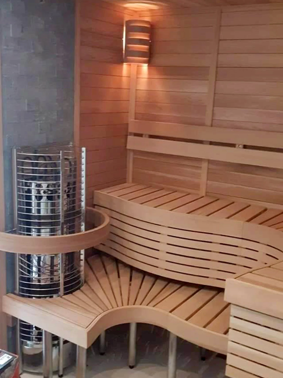 Cedar sauna with a curved bench, tower heater, and a warm wall sconce