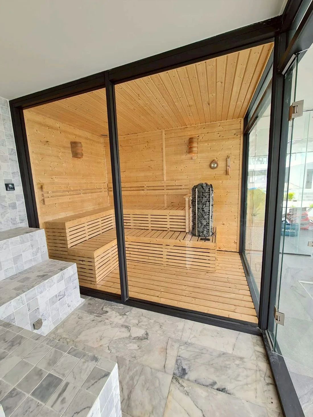 Indoor sauna with a full glass wall, marble floor, and tower heater