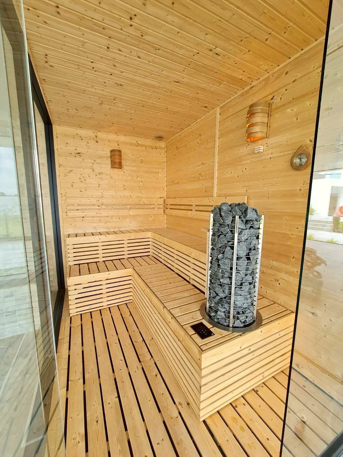 Sauna interior with a tower heater set into the bench platform beside a glass wall