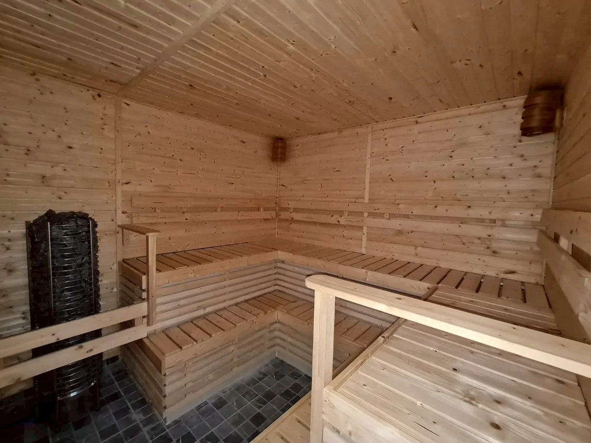 Pale timber sauna interior with a black stone-filled tower heater, two bench tiers, and a slate mosaic floor
