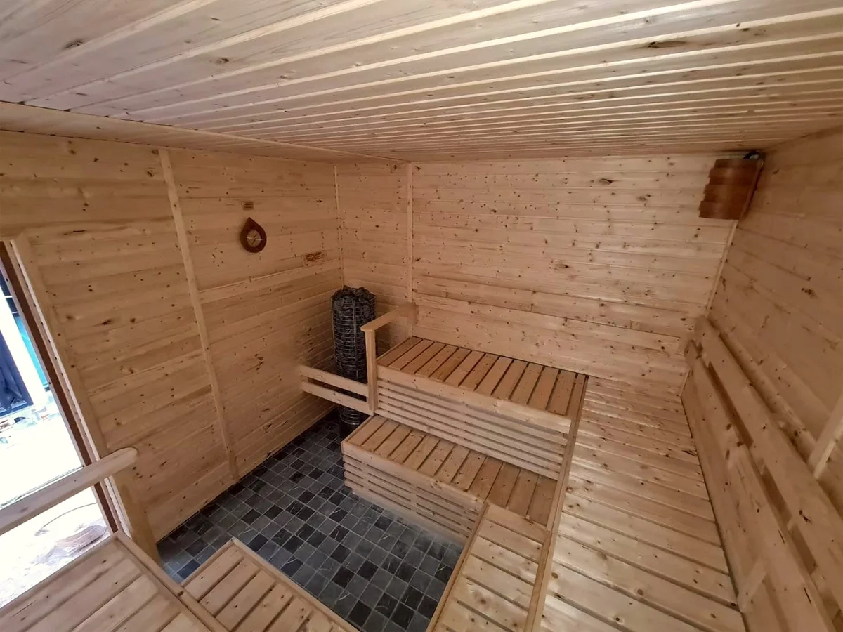 Pale timber sauna interior with a black stone tower heater in the corner and tiered benches above a slate floor