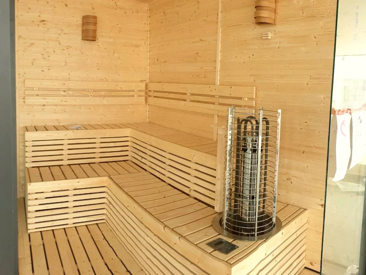Pale timber sauna interior with a stainless open-frame tower heater rising through the bench platform