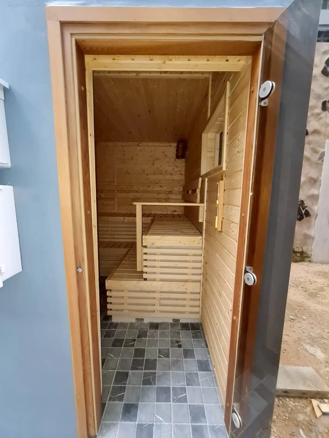 Small timber sauna seen through its open door, slate tile on the floor