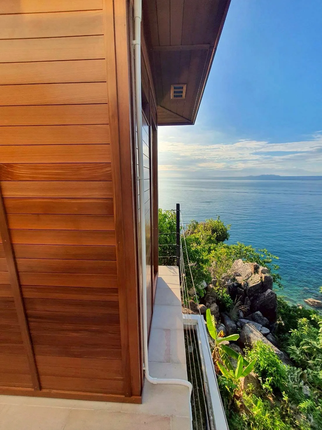 Cedar sauna cabin standing above a rocky shoreline in southern Thailand