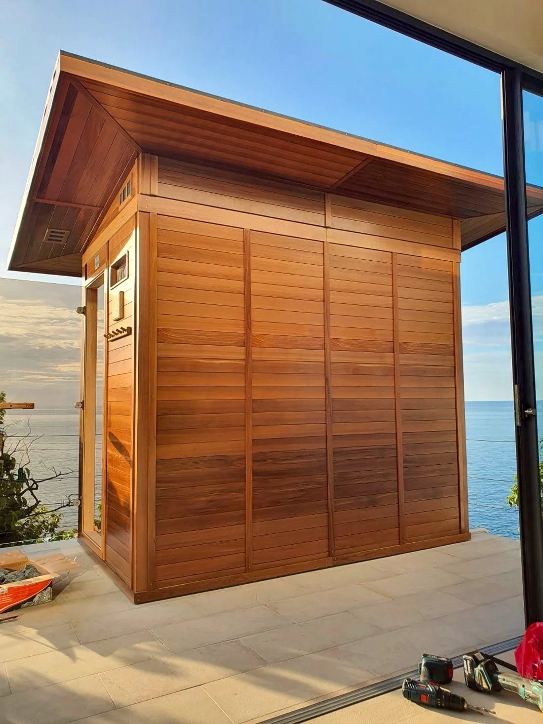 Side elevation of the seaside cedar sauna cabin against the open sea