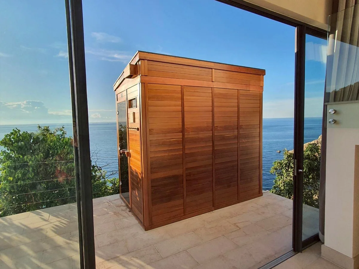 View through the open glass door of the clifftop cedar cabin toward the terrace and the open sea