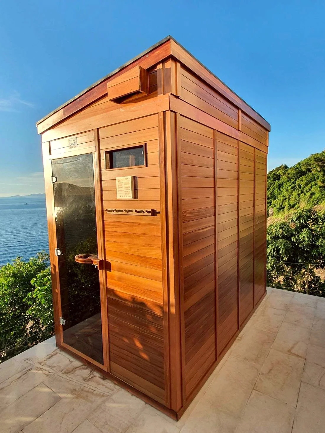 Seaside cedar sauna cabin with a black glass door, photographed in portrait